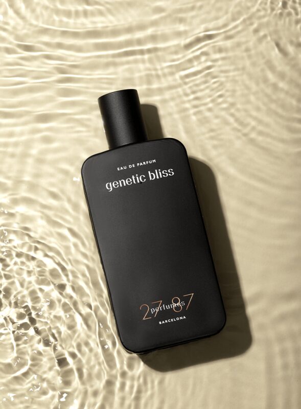 zwarte parfumfles van het merk 2787 Perfumes liggend in ondiep helder water op het strand